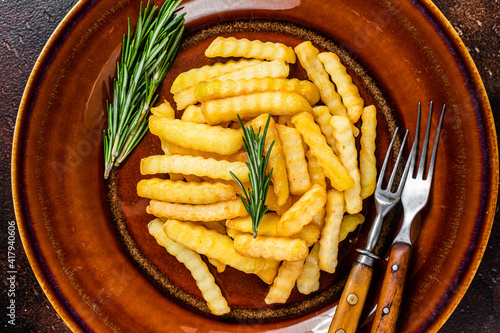 Fried Crinkle French fries potatoes or chips  in a rustic plate. Dark background. Top view