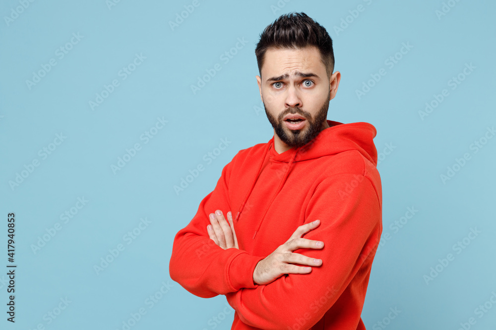 Young caucasian indignant bearded attractive handsome student man 20s in casual red orange hoodie hold hands crossed folded isolated on blue color background studio portrait People lifestyle concept Young caucasian indignant bearded attractive handsome student man 20s in casual red orange hoodie hold hands crossed folded isolated on blue color background studio portrait People lifestyle concept