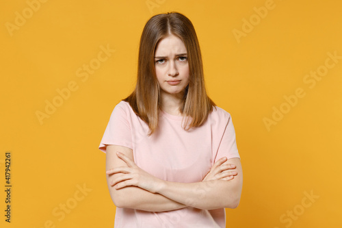Young disappointed serious sad caucasian woman 20s in casual basic pastel pink t-shirt, blank print design look camera hold hands crossed folded isolated on yellow color background studio portrait