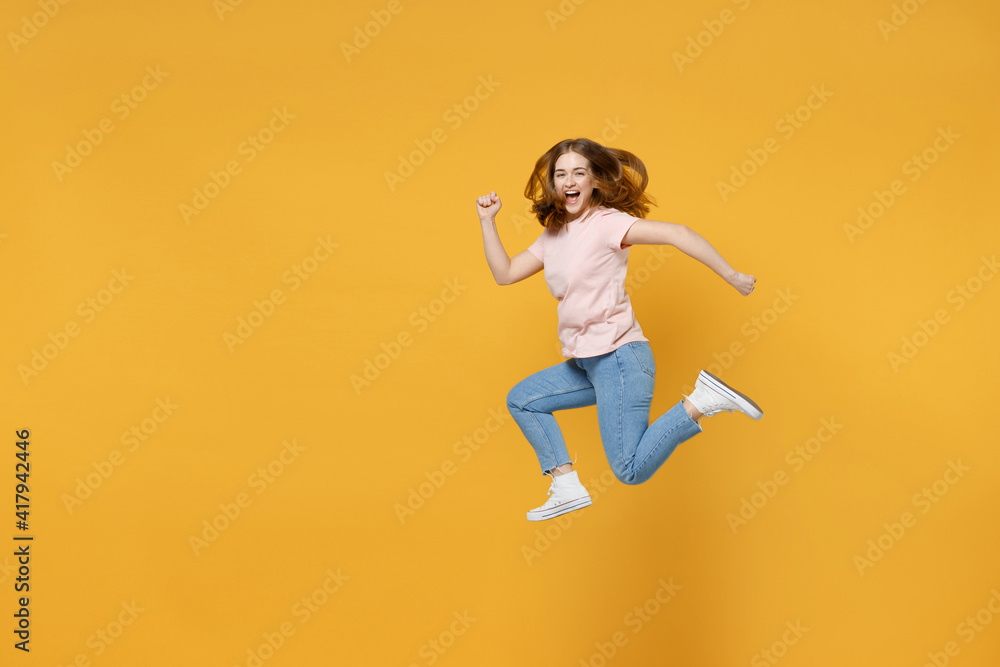 Full length of young sportive energetic caucasian hurrying up woman 20s wearing basic pastel pink t-shirt jumping high runnig fast look camera isolated on yellow color background studio portrait.