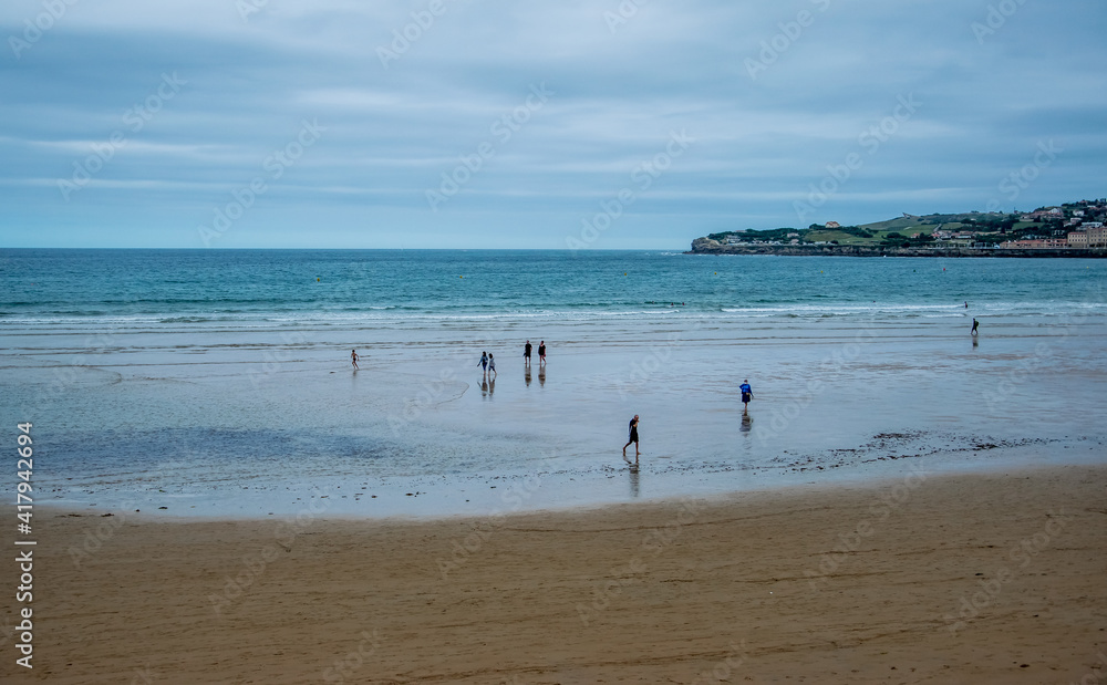 Unas pocas personas pasean por una playa del norte de España durante un día lluvioso de verano