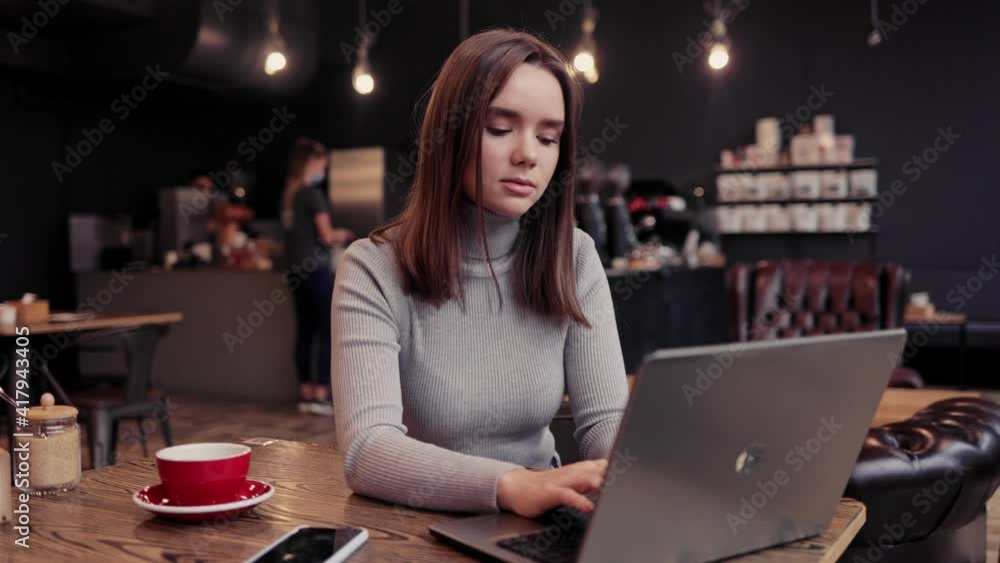 Young female freelancer working with laptop sitting in coffee shop. Texting messages, browsing internet, searching information, studying online. Online education, remote working, courses online Young female freelancer working with laptop sitting in coffee shop. Texting messages, browsing internet, searching information, studying online. Online education, remote working, courses online
