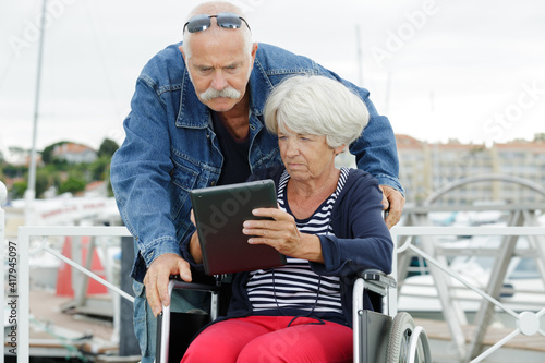 senior man helping wife in wheelchair with tablet