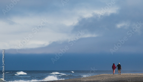 A man and woman holding hands and walking on the beach at Neskown on the Oregon coast.