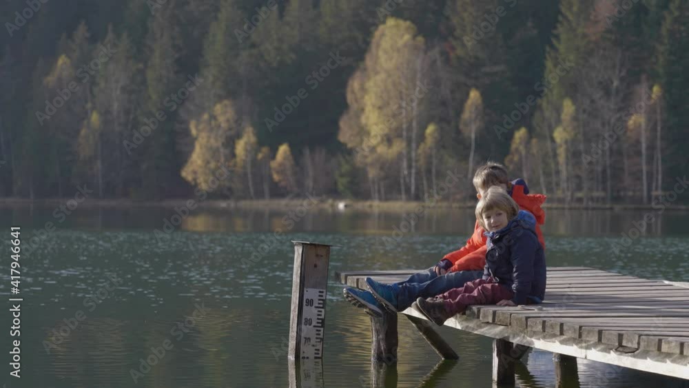 Two brothers sitting on wooden pontoon over lake, autumn scenery Two brothers sitting on wooden pontoon over lake, autumn scenery
