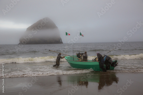 Launching a dory fishing boat from the beach at pacific City on the Oregon coast with Haystack rock in background on a foggy morning