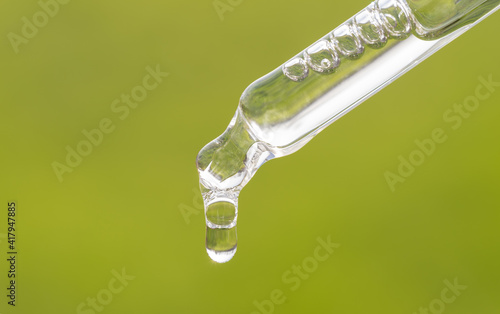 Pipette with essential oil, serum, hyaluronic acid on grass background. Aromatherapy, alternative medicine with green leaf. Closeup of green pippette, falling drop close up. Beauty skin care product photo
