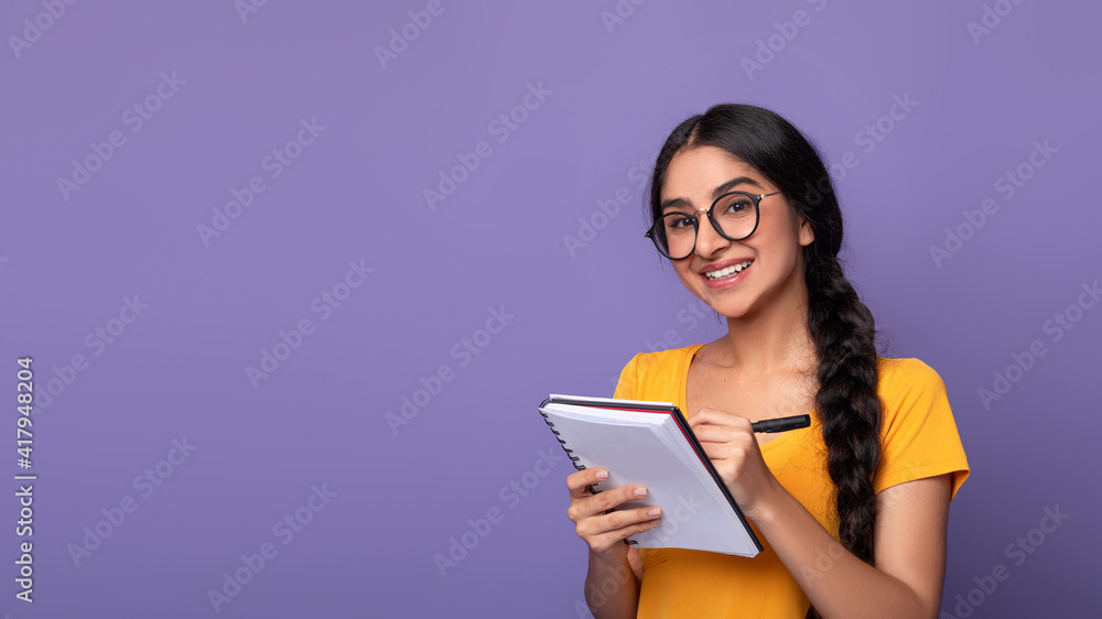 Indian woman holding pen writing in notebook at studio Indian woman holding pen writing in notebook at studio