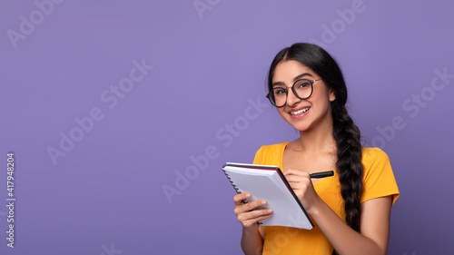 Indian woman holding pen writing in notebook at studio