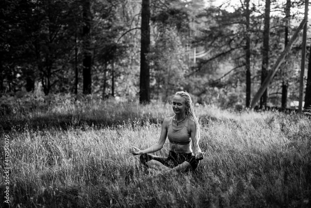 An yoga woman meditating on a picturesque glade in the forest. Black and white photo.
