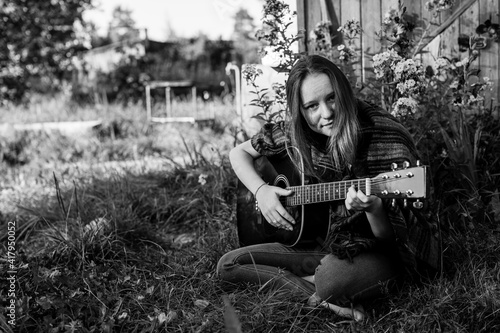 Girl playing acoustic guitar sitting outdoors. Black and white photo.