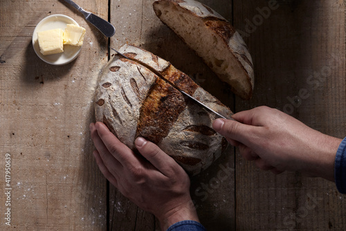 Photo Close up of man cutting homemade sourdough bread loaf on wood table