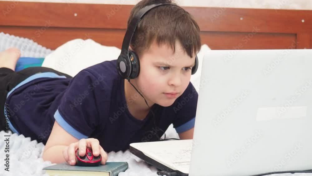 young boy playing in his computer or tablet and sitting in the bed. online games, stream or undergoes online training, online courses, studies at home during quarantine young boy playing in his computer or tablet and sitting in the bed. online games, stream or undergoes online training, online courses, studies at home during quarantine