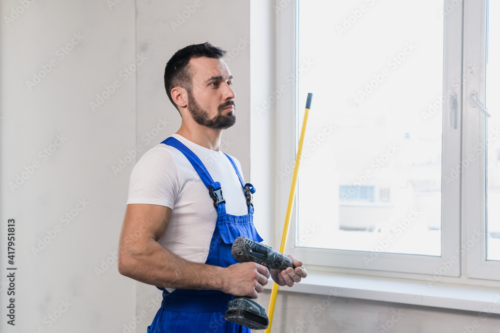 A man in a blue overalls holds a tape measure in his hand A man in a blue overalls holds a tape measure in his hand