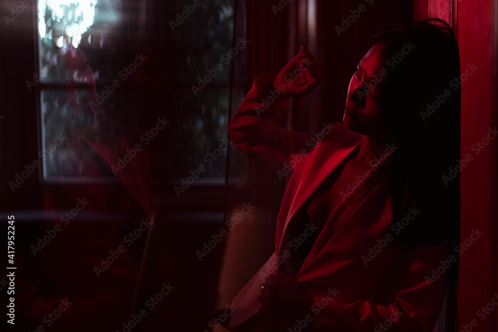Young woman shielding face while standing in low red light at home Young woman shielding face while standing in low red light at home