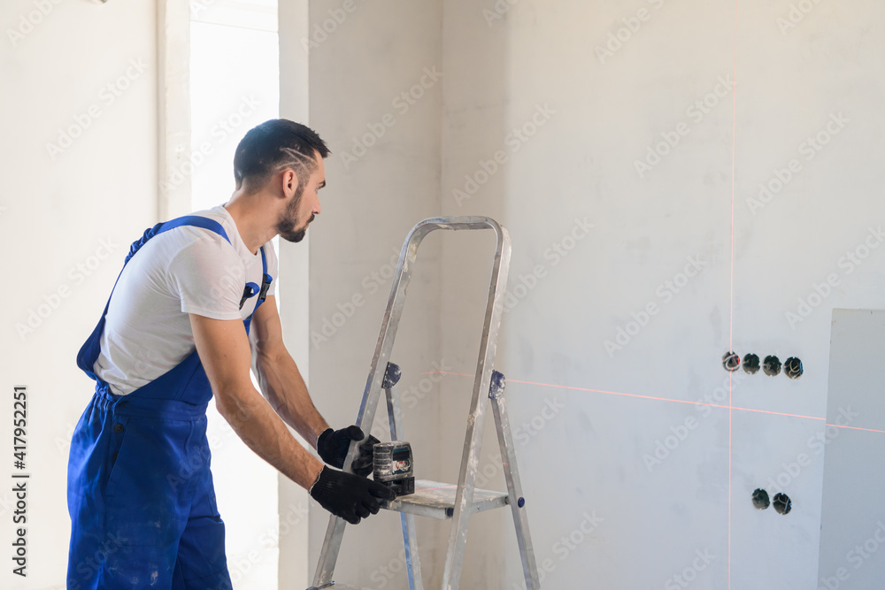 A electrician in uniform uses an electronic ruler to mark the wall