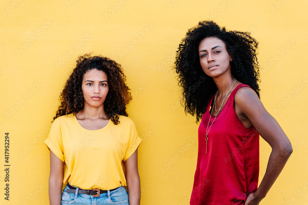 Confident lesbian couple standing against yellow wall Confident lesbian couple standing against yellow wall