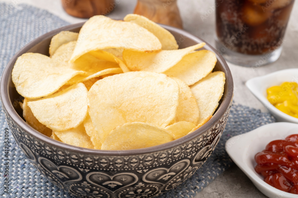 Potato chips in a bowl, pepper, salt, mustard, ketchup and a glass of soda Potato chips in a bowl, pepper, salt, mustard, ketchup and a glass of soda