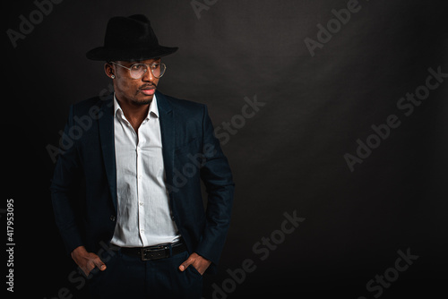 Portrait of attractive, handsome, pretty, serious and stylish professional african american businessman executive with stylish suit and white shirt and black hat isolated on dark background. Low key. 