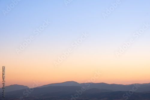 Beautiful sunset sky, blue at the top and golden orange above the shilouette horizon mountains