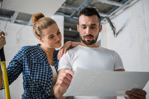 A woman holds a roller in her hand and hugs a man. They look at the apartment layout photo