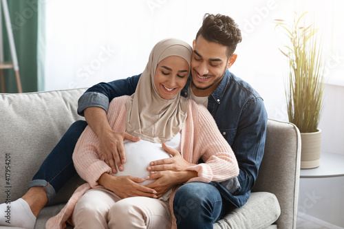 Happy Pregnant Muslim Couple Relaxing On Couch At Home