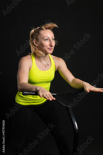 Girl on a fitness trampoline on a black background in a yellow t-shirt jump, fun exercise fitness lifestyle leap, weight rebounder. Wellness center motion, young muscle instructor enjoy