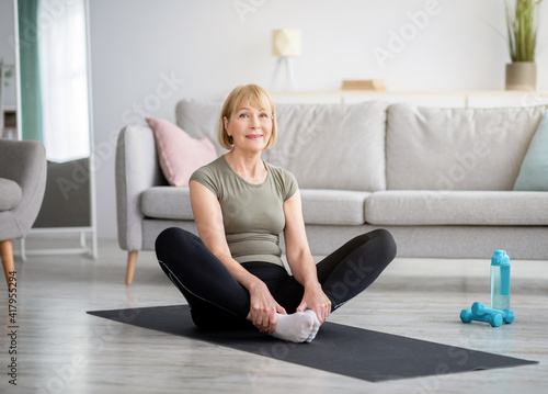 Canvas Print Attractive fit mature lady sitting in butterfly yoga pose on sports mat at home, copy space