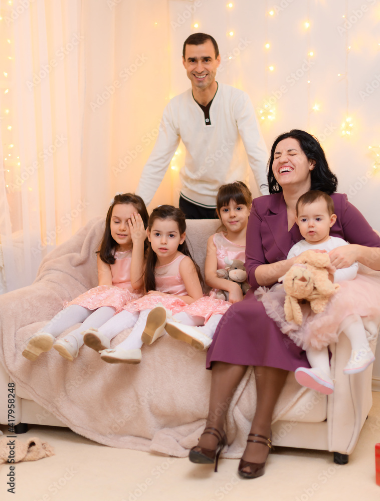 family portrait of a parents and children, sitting on a couch in home interior decorated with lights family portrait of a parents and children, sitting on a couch in home interior decorated with lights
