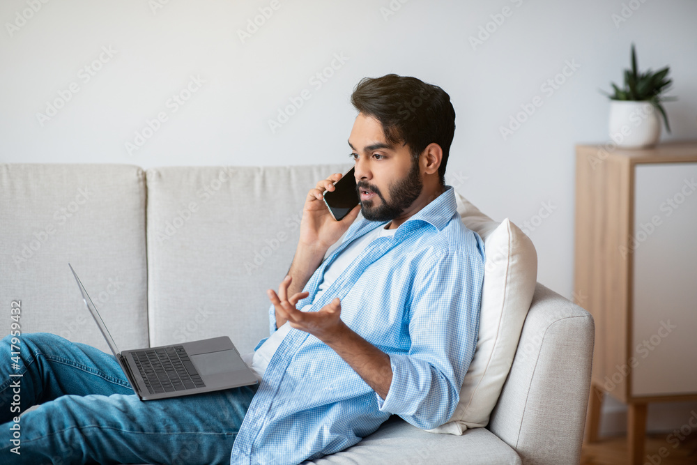 Arab Man Having Problem While Working With Laptop And Cellphone At Home