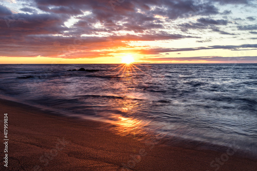 An epic sunset over a tropical beach with clouds and sunstar.