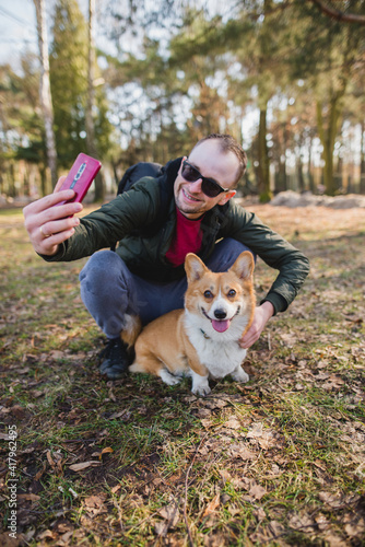 a  young man doing a selfie with a welsh corgi pembroke dog during a walk in a park © Justyna