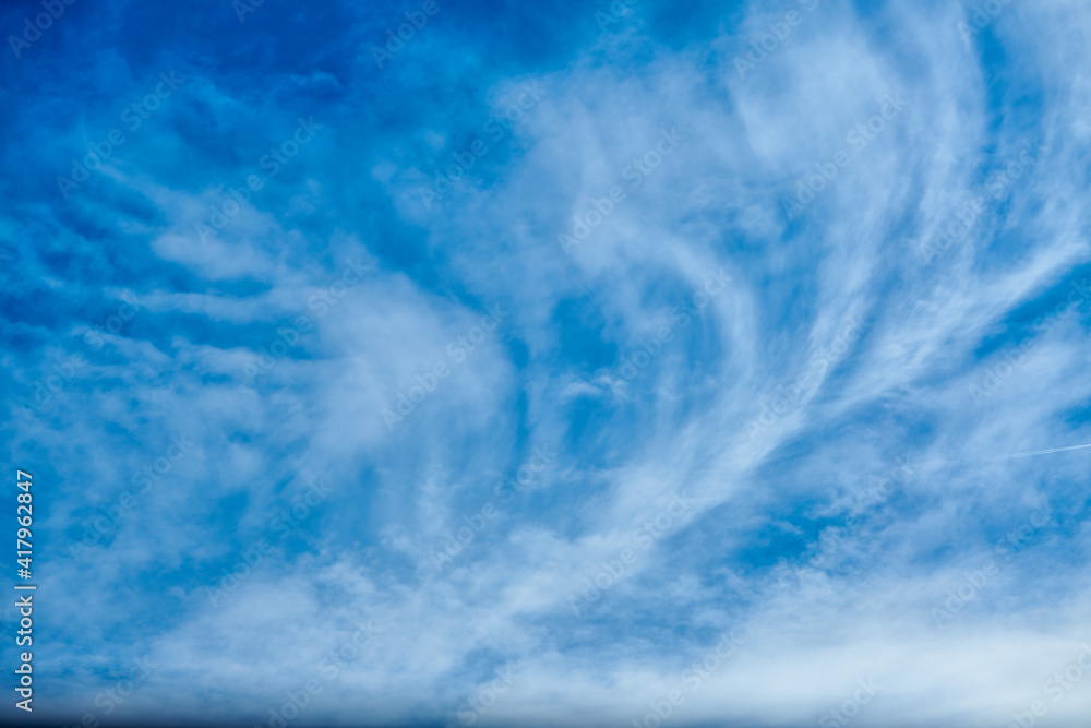 High white wispy cirrus clouds expanding by wind to cover deep navy blue sky in summer sunny day. Abstract sky background