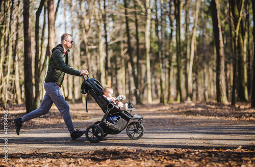 a young male jogging in a park with a baby stroller 