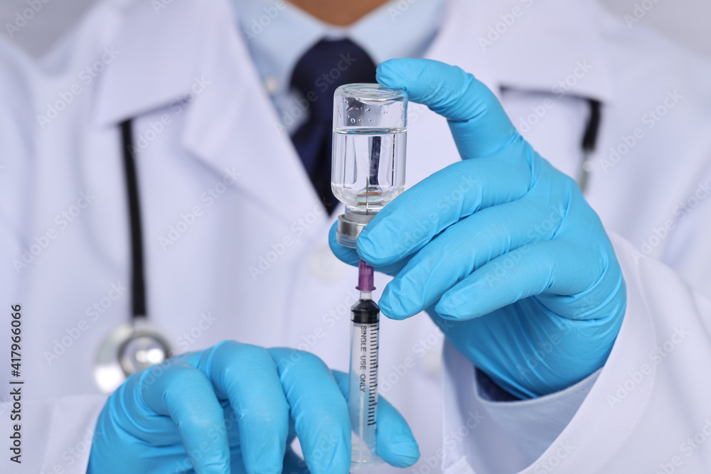 Male doctor hands on blue gloves with stethoscope on shoulder holding syringe and Covid-19 coronavirus vaccine vial or drug on white background. Healthcare And Medical concept Male doctor hands on blue gloves with stethoscope on shoulder holding syringe and Covid-19 coronavirus vaccine vial or drug on white background. Healthcare And Medical concept