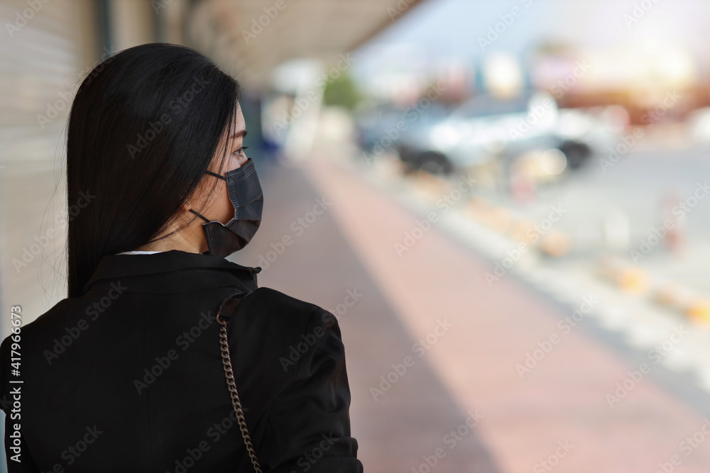 Rear view young asian business woman in business black suit with protect mask for healthcare walking on street public outdoor and looking way. New normal and social distancing concept Rear view young asian business woman in business black suit with protect mask for healthcare walking on street public outdoor and looking way. New normal and social distancing concept