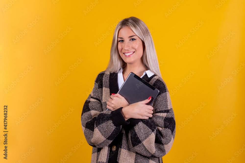 Portrait of a young woman holding digital tablet isolated on a yellow background - Laughing influencer girl with a tablet computer in hand uses technology and looking at camera Portrait of a young woman holding digital tablet isolated on a yellow background - Laughing influencer girl with a tablet computer in hand uses technology and looking at camera