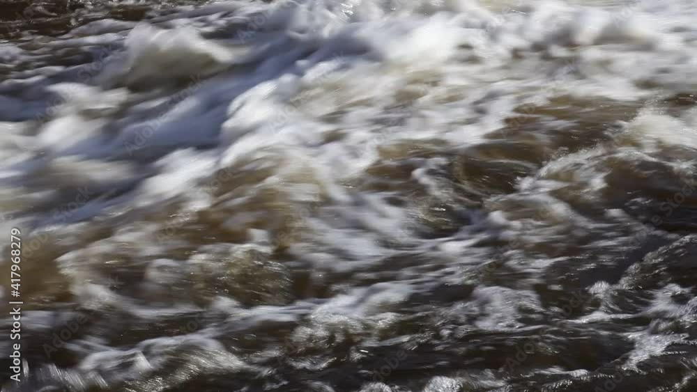 Closeup monotonous powerful fast bubbling water stream from a storm drain spillway, water flow from left to right Closeup monotonous powerful fast bubbling water stream from a storm drain spillway, water flow from left to right