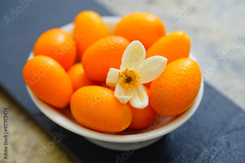 Little dish of small kumquat fruit with a fresh citrus flower