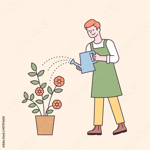 A man in an apron is holding a watering can and watering a flower pot. flat design style minimal vector illustration.