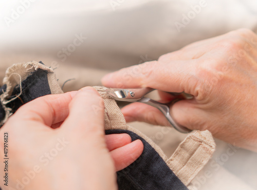 Seamstress crop excess of sticking out threads workpiece from clothing by using small scissors. Process of crafting of clothes