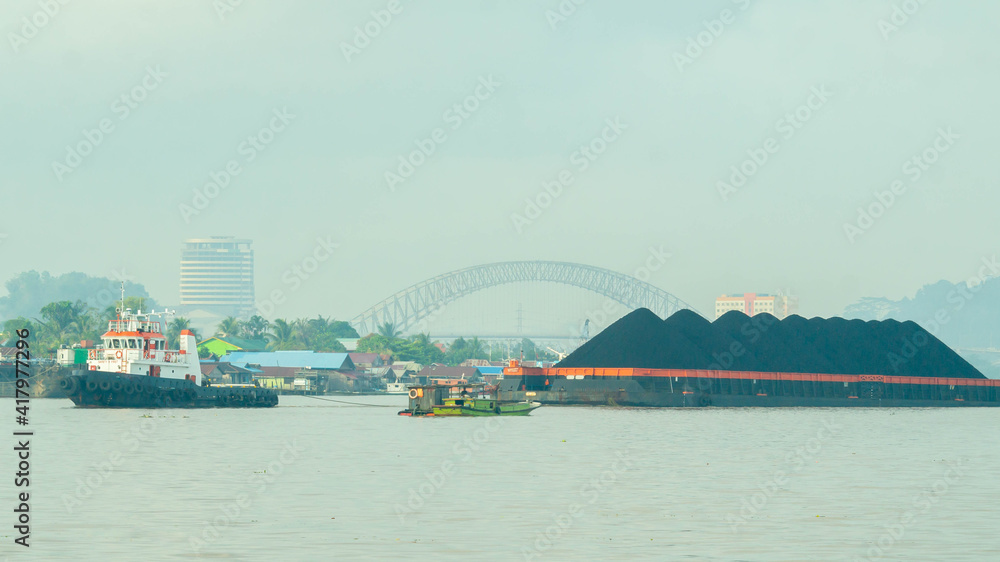 Tugboat drag barge full of coal crossing Mahakam River, Samarinda, in the morning. Transportation and industrial background