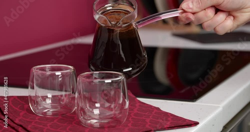 Woman pouring hot coffee from jezve in glasses on kitchen counter photo