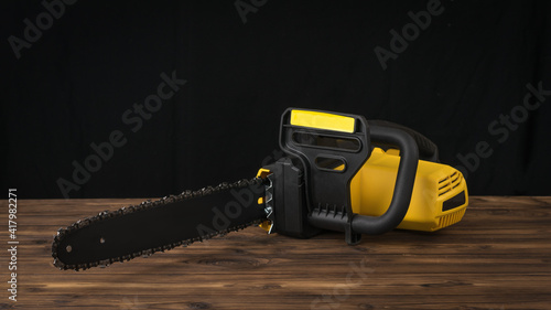 Black and yellow electric saw on a wooden table on a black background.