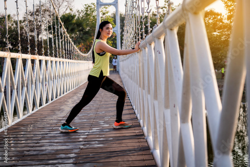 A young Asian woman runner athlete in sports outfit doing stretching and warm up before workout, jogging and fitness training session in the city park in the morning. Sports and recreation