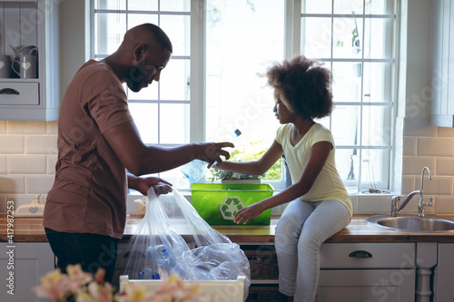 African american girl and her father sorting recycling together in kitchen photo