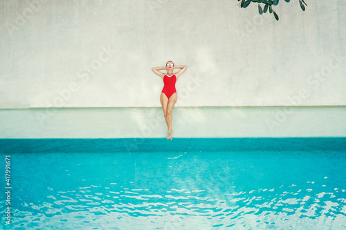 Enjoying suntan and vacation. Top view of pretty young woman in red swimsuit lying near swimming pool. © luengo_ua