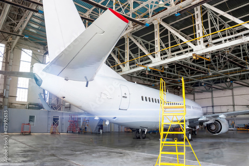White passenger aircraft in the hangar. Airplane under maintenance. Checking mechanical systems for flight operations
