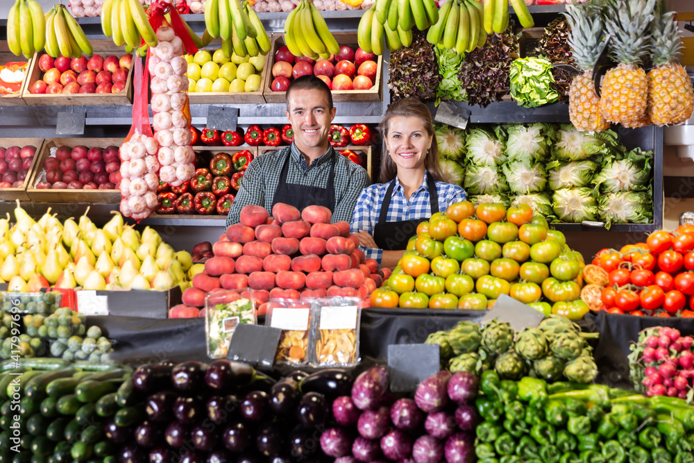 Friendly man and woman vegetable shop sellers posing behind a counter