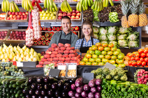 Friendly man and woman vegetable shop sellers posing behind a counter